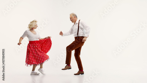 Elderly man and woman share joyful dance in retro-inspired outfits isolated on white background. Elegance of classic swing dance. Concept of retro dance, hobby, aging, active lifestyle photo