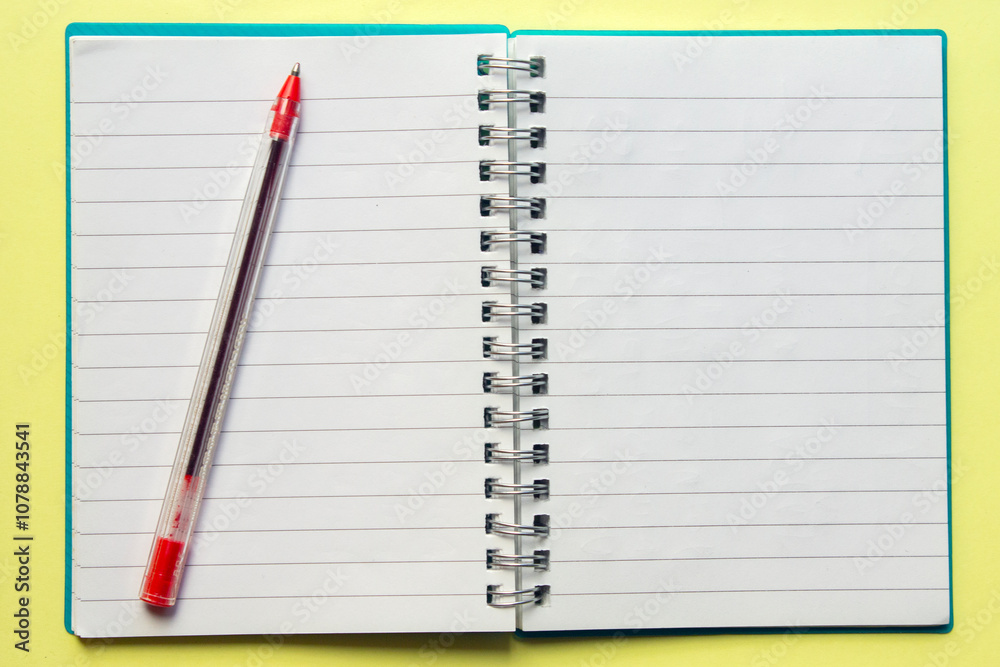 open spiral notebook with a red pen on , on yellow background. top view open spiral notebook with a red pen on , on yellow background. top view