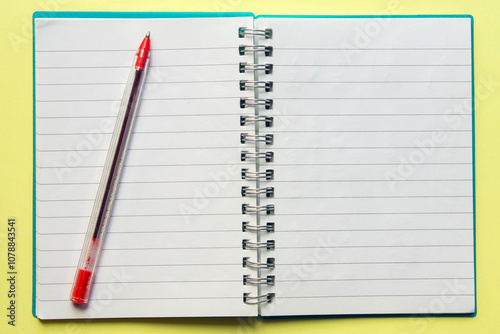 open spiral notebook with a red pen on , on yellow background. top view