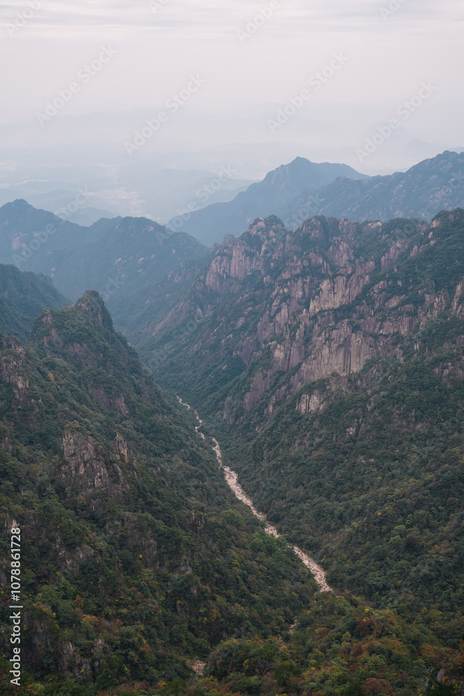 Fototapeta premium Aerial view of a valley with a dry river and a Chinese city in the background that almost cannot be seen due to the fog and air pollution, autumn in the Yellow Mountain, Huangshan, China