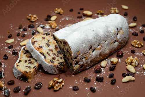 Traditional cake Stollen dusted with powdered sugar with dried fruits and nuts on a brown background.