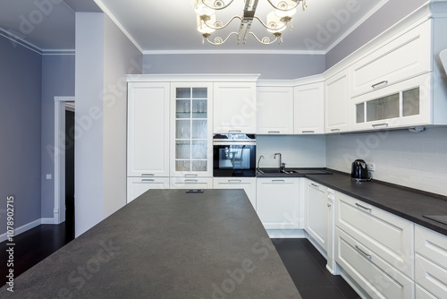 Light kitchen interior with island in suburban home. Stylish kitchen with dark stone countertops.