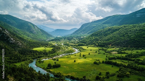 Aerial View of Serene Green Valley with River Flowing through Lush Landscape Surrounded by Majestic Mountains Under Cloudy Sky