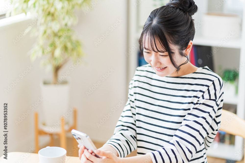 部屋でスマホを操作する若い女性。
部屋でスマホを操作する若い女性。