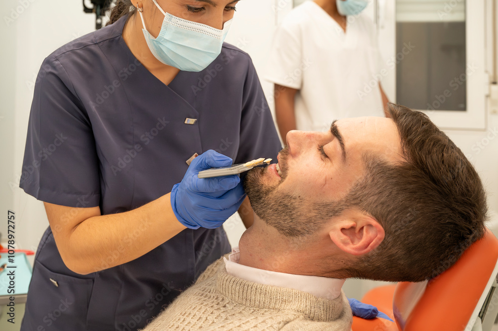 Fototapeta premium Dental technician selecting tooth shade for male patient in clinic
