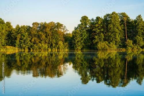 Quiet lake surrounded by forest, reflection of trees on water surface. clear sunny day. Photo wallpaper. Beauty of nature.