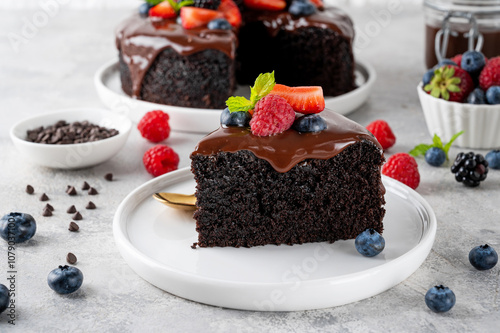 Delicious chocolate cake with chocolate glaze and fresh berries on a white plate on a gray concrete background. photo