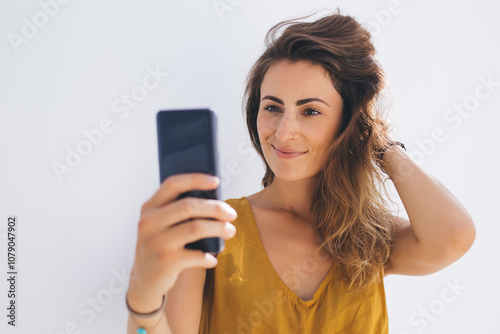 Smiling gorgeous lady in modern outfit capturing selfie photo by mobile on gray blank background photo