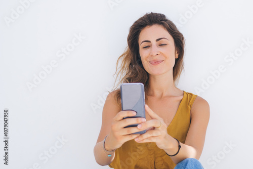 Pleased female in casual wear taking selfie on white wall photo