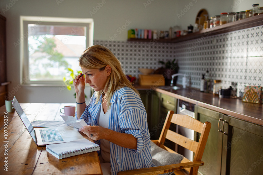 Woman working on finances at home with a laptop and bills Woman working on finances at home with a laptop and bills