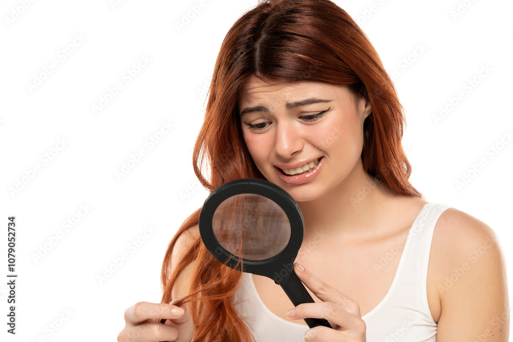 Worried redhead woman inspecting her hair with a magnifying glass on a white background Worried redhead woman inspecting her hair with a magnifying glass on a white background