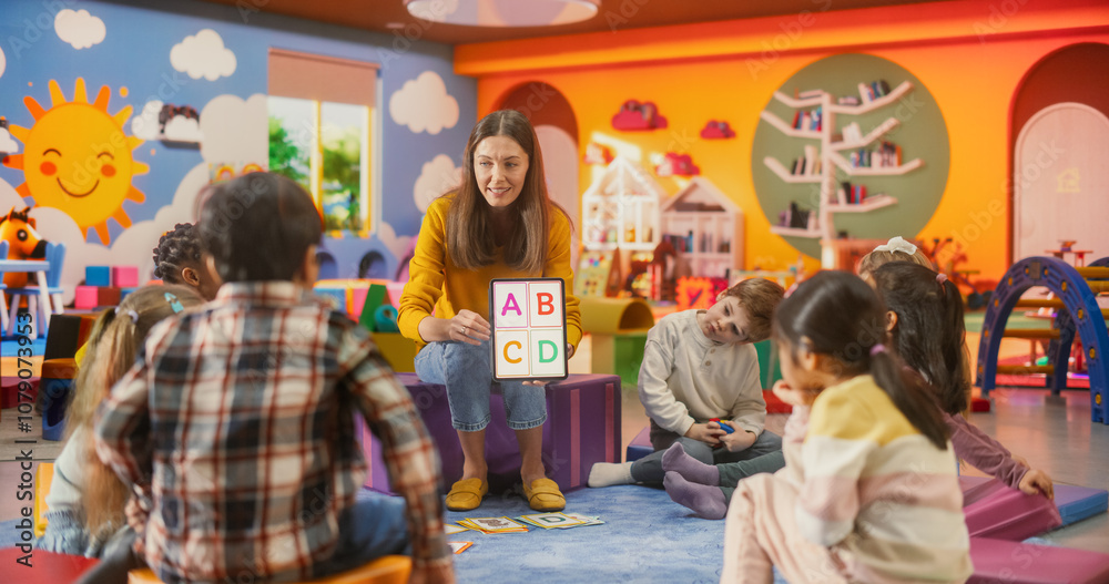 Happy Professional Kindergarten Teacher Using Tablet Computer to Show Numbers and Alphabet Characters to Smart Little Kids at a Modern Colorful Kindergarten. Female Educator Developing Social Skills Happy Professional Kindergarten Teacher Using Tablet Computer to Show Numbers and Alphabet Characters to Smart Little Kids at a Modern Colorful Kindergarten. Female Educator Developing Social Skills