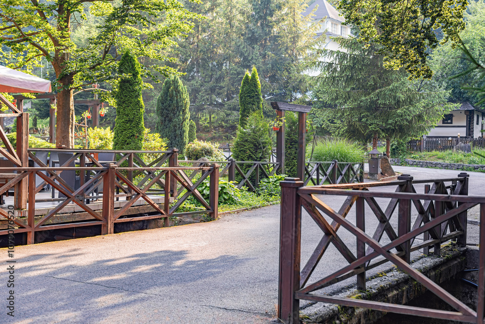 Wooden fences line a charming path through a lush, green garden. Tall trees and vibrant plants create a peaceful, natural setting. Wooden fences line a charming path through a lush, green garden. Tall trees and vibrant plants create a peaceful, natural setting.
