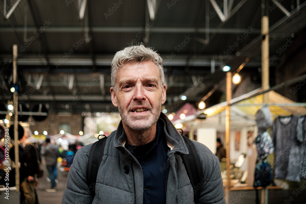 Grey-haired man smiling in a crowded indoor market wearing a backpack Grey-haired man smiling in a crowded indoor market wearing a backpack