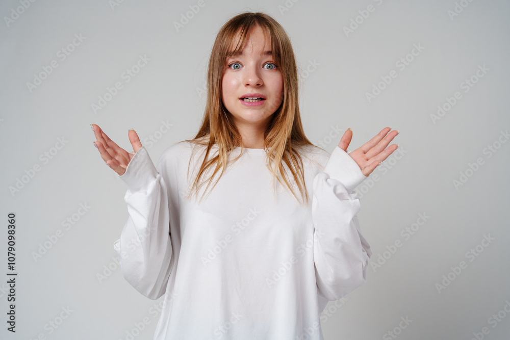 A surprised child wearing a white long-sleeve shirt and blue jeans expresses confusion in a studio setting A surprised child wearing a white long-sleeve shirt and blue jeans expresses confusion in a studio setting