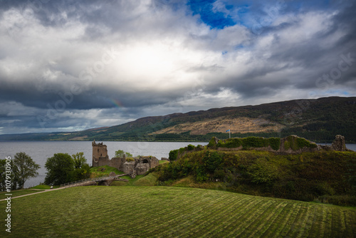 Ruined Urquhart Castle in the Highlands of Scotland besides Loch Ness lake in background with dramatic sky and part of rainbow. photo