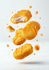 Golden crispy chicken nuggets in mid-air with flying crumbs against white background