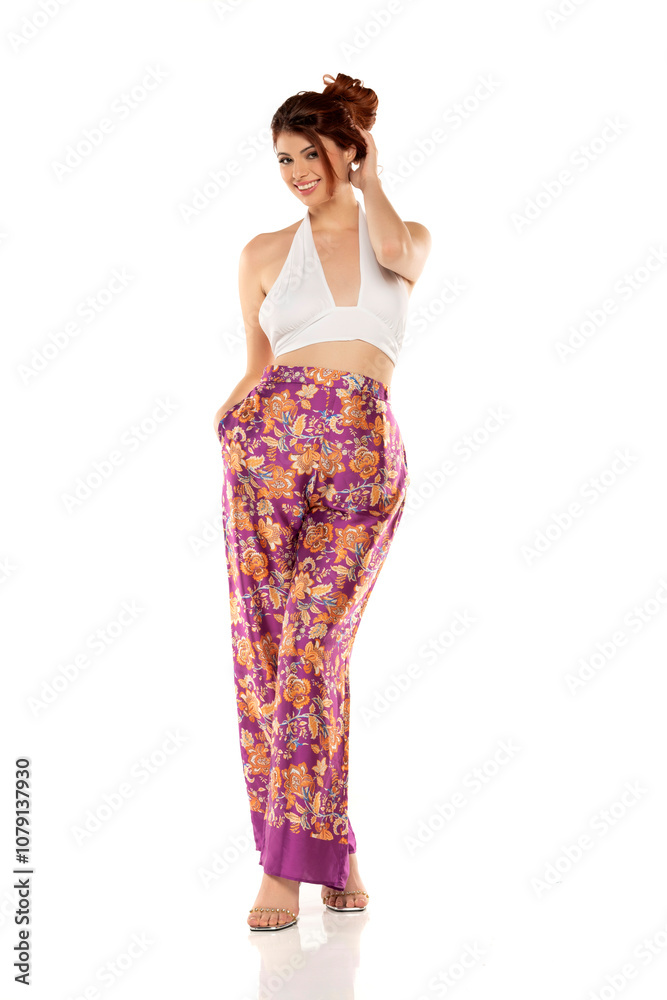 Fashion style studio portrait of beautiful young woman. Floral pattern wide leg pants and white sleevles shirt. Model standing and posing against white background Fashion style studio portrait of beautiful young woman. Floral pattern wide leg pants and white sleevles shirt. Model standing and posing against white background