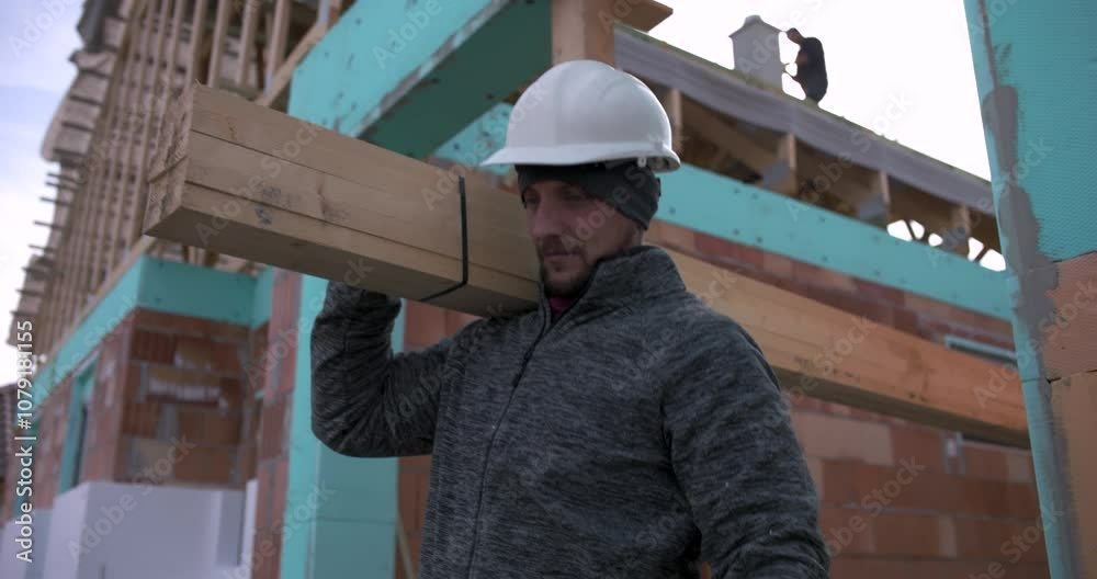 Carpenters carrying long wooden beams at construction site, teamwork in house building project, two workers in hard hats and gloves, residential construction, building materials