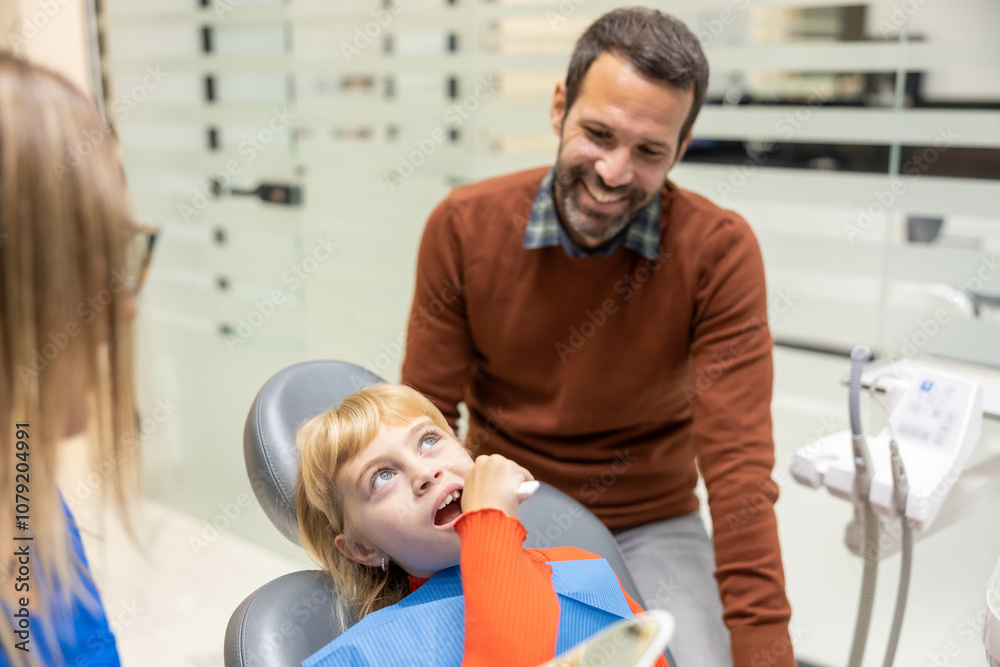 A child sits in a dentist chair, wearing a dental bib, while a smiling adult stands beside them in a modern dental office, suggesting a comforting environment. A child sits in a dentist chair, wearing a dental bib, while a smiling adult stands beside them in a modern dental office, suggesting a comforting environment.