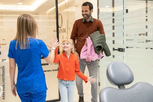 A cheerful young girl high-fives a smiling dentist in a modern dental office, celebrating a successful dental visit with her parent looking on happily.