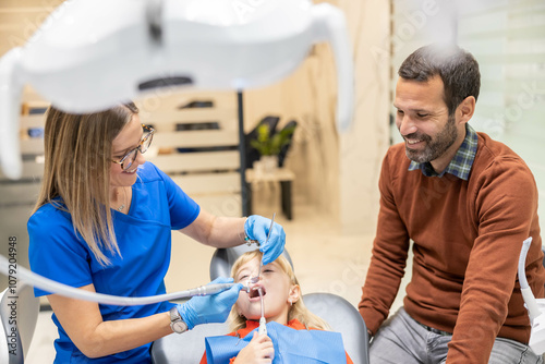 Father smiles observing child's dental treatment, capturing a moment of parental reassurance and comfort in a modern clinical dental environment. photo