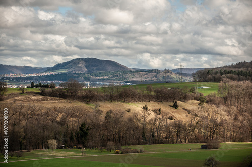 Bergkette der schwäbischen Alb mit Grünfläche in Flusstal mit Hang und Bäumen und Lichtfleck von Sonne   und Wolkenhimmel photo