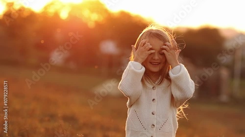 Adorable cheerful child girl 5-6 years smiling runs and looks to camera outdoors on sunset. Kid in casual clothing has fun enjoy relaxing on nature on autumn holiday vacation. Happy childhood concept