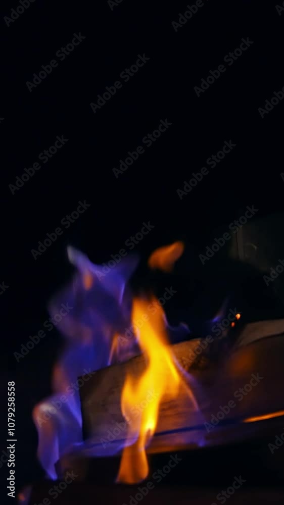 Blue and yellow fire flame burning in a stone fireplace. Wooden logs are burning in darkness. Cozy and warm atmosphere. Vertical video Blue and yellow fire flame burning in a stone fireplace. Wooden logs are burning in darkness. Cozy and warm atmosphere. Vertical video