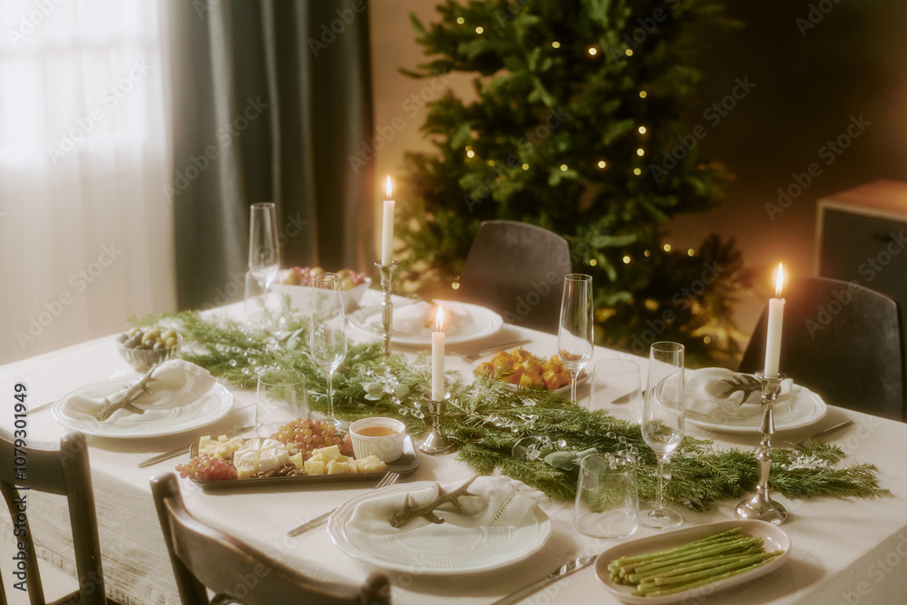Fototapeta premium High angle shot of decorated table with appetizers, fur tree with golden lights in dining room