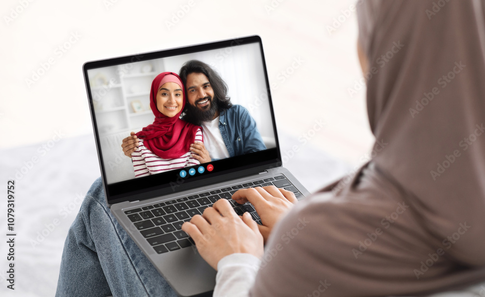 A woman in a headscarf smiles while video chatting with her friends, capturing a moment of connection and laughter from the comfort of her home on a bright afternoon. A woman in a headscarf smiles while video chatting with her friends, capturing a moment of connection and laughter from the comfort of her home on a bright afternoon.