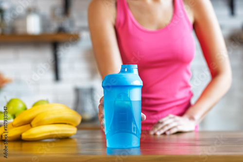 Obraz na płótnie Woman holding a blue shaker bottle in a kitchen. Concept of healthy living, fitness, and nutrition w salonie