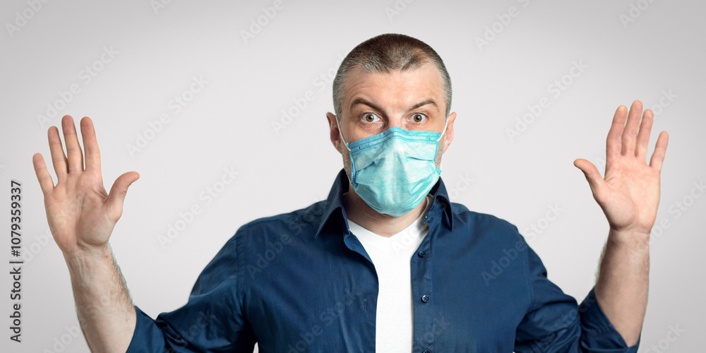 Man In Medical Mask Raising Hands Posing On Gray Background During Covid-19 Pandemic Outbreak. Studio Shot, Panorama Man In Medical Mask Raising Hands Posing On Gray Background During Covid-19 Pandemic Outbreak. Studio Shot, Panorama
