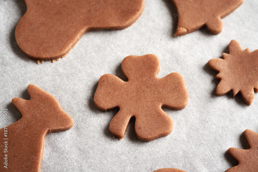 Shapes cut out from raw pastry dough on a sheet of baking paper - preparation of gingerbread Christmas cookies Shapes cut out from raw pastry dough on a sheet of baking paper - preparation of gingerbread Christmas cookies