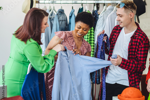 Group of friends generation z girls and boys enjoying shopping in a second hand store or swap home party, trying hats, jackets, vintage brand clothes. Flea market, bargain hunting. Sustainable fashion photo