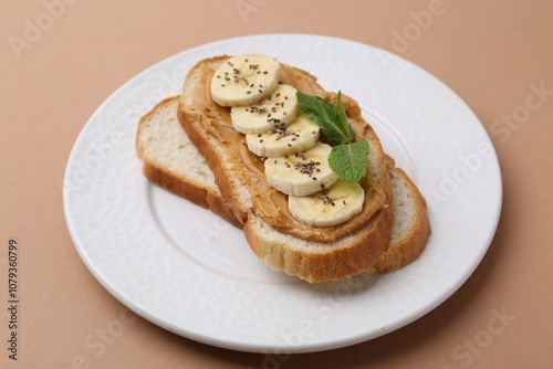 Tasty sandwich with peanut butter, banana, chia seeds and mint on brown background, closeup