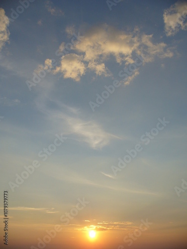 Blue sky with yellow sun during sunset and small clouds - natural sunny background. Topics: weather, sun energy, season, beauty of nature, dusk, evening