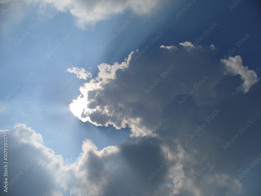 Natural blue and white sky background with sun rays coming out from behind clouds. Topics: weather, meteorology, sun energy, season, beauty of nature, air space Natural blue and white sky background with sun rays coming out from behind clouds. Topics: weather, meteorology, sun energy, season, beauty of nature, air space