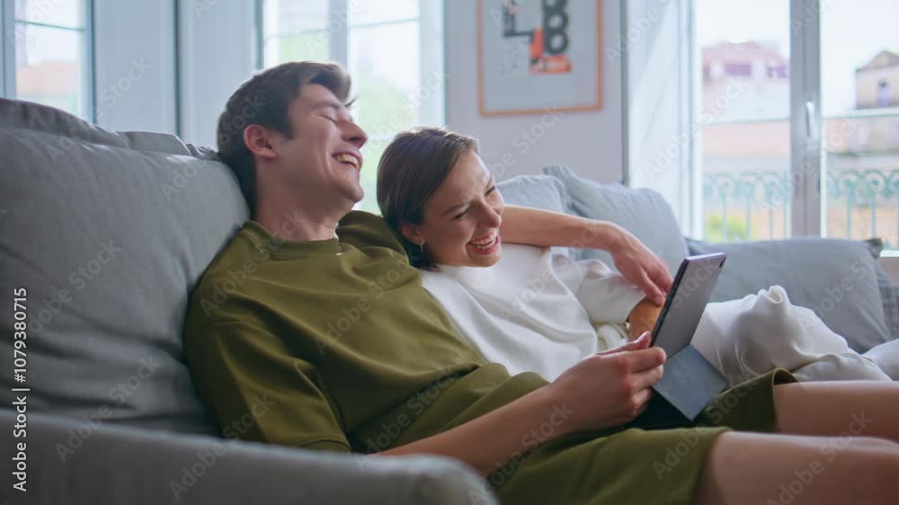 Embracing lovers using tablet laughing at home closeup. Positive couple cuddling Embracing lovers using tablet laughing at home closeup. Positive couple cuddling
