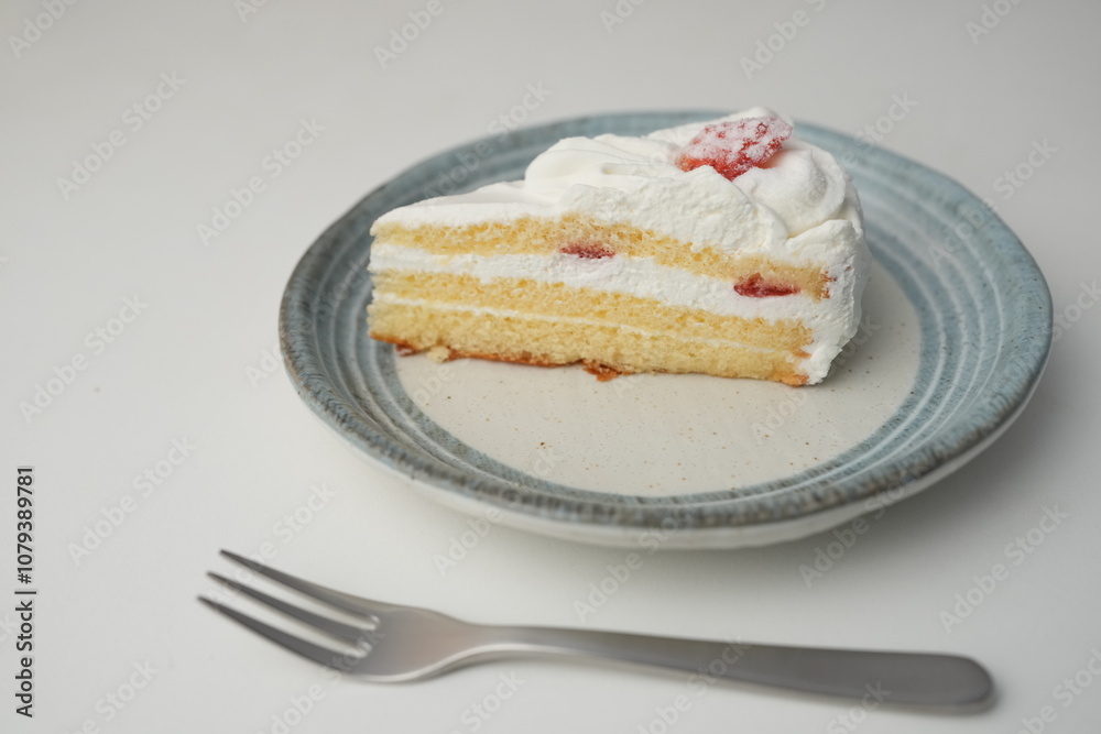 One small Japanese strawberry shortcake and a small fork on a stylish Japanese plate on a white table One small Japanese strawberry shortcake and a small fork on a stylish Japanese plate on a white table