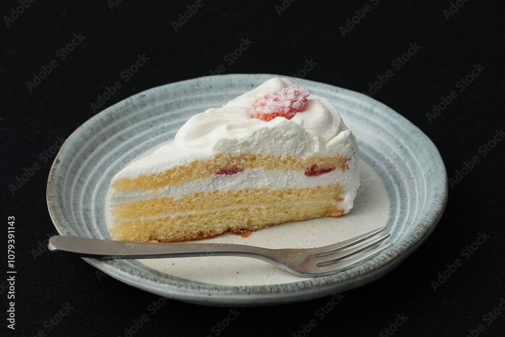 One small Japanese strawberry shortcake and a small fork on a stylish Japanese plate on a black cloth on a white table One small Japanese strawberry shortcake and a small fork on a stylish Japanese plate on a black cloth on a white table