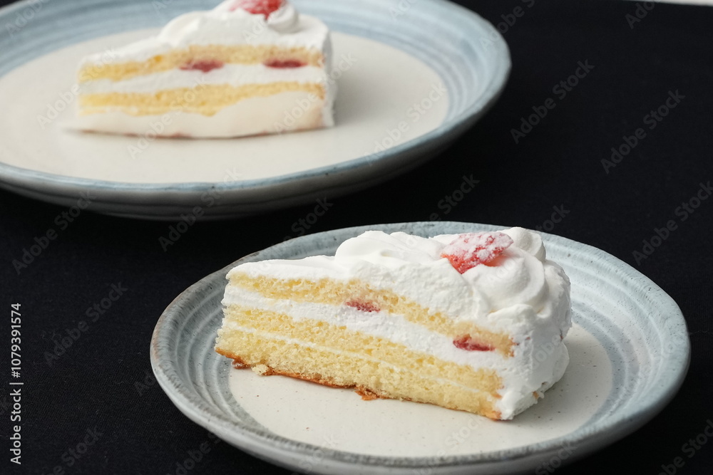 Small Japanese strawberry shortcakes on two stylish Japanese style plates, each on a black cloth on a white table. Small Japanese strawberry shortcakes on two stylish Japanese style plates, each on a black cloth on a white table.