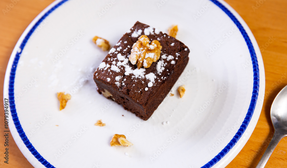 Piece of delicious brawny with walnuts served in a ceramic plate with teaspoon on the table