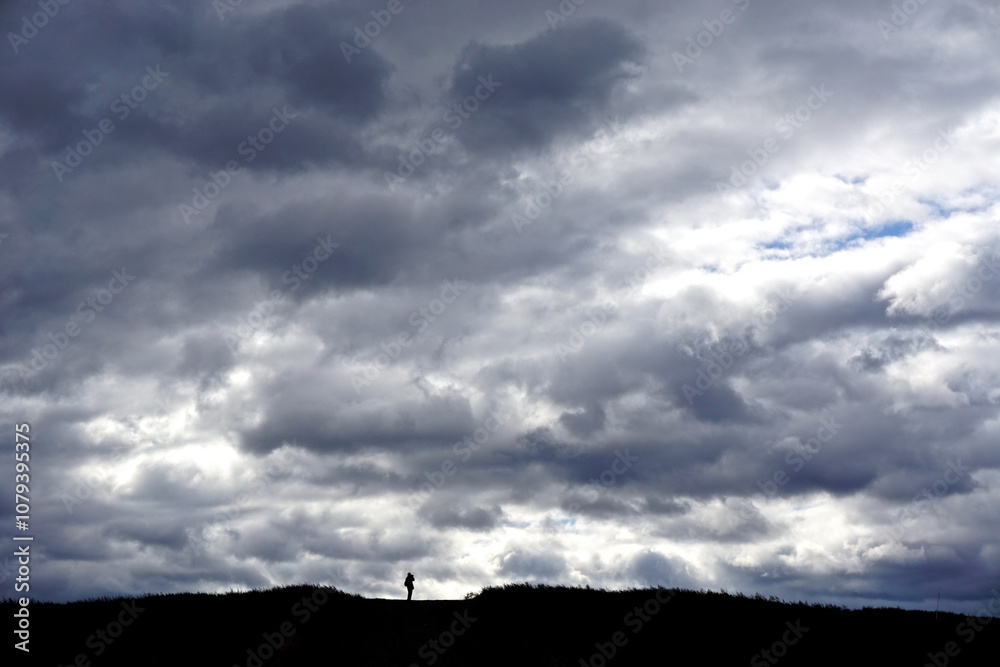 Croton-on-Hudson, New York: The silhouette of one person on a path at the top of a hill under a dramatic cloud formation, in Croton Point Park, Westchester County. Croton-on-Hudson, New York: The silhouette of one person on a path at the top of a hill under a dramatic cloud formation, in Croton Point Park, Westchester County.