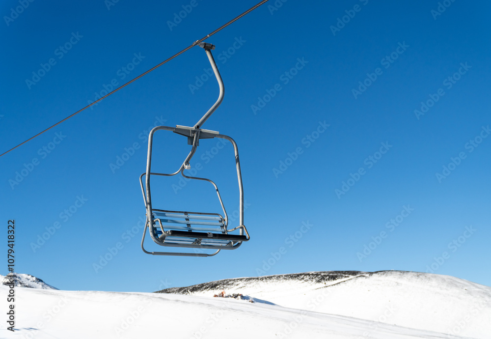 An empty chairlift suspended over a snowy landscape, capturing the peacefulness of a winter day in the mountains, with untouched snow below.