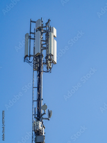 Cellular base station tower with antennas and microwave dishes providing wireless communication services against a clear blue sky ensures seamless connectivity