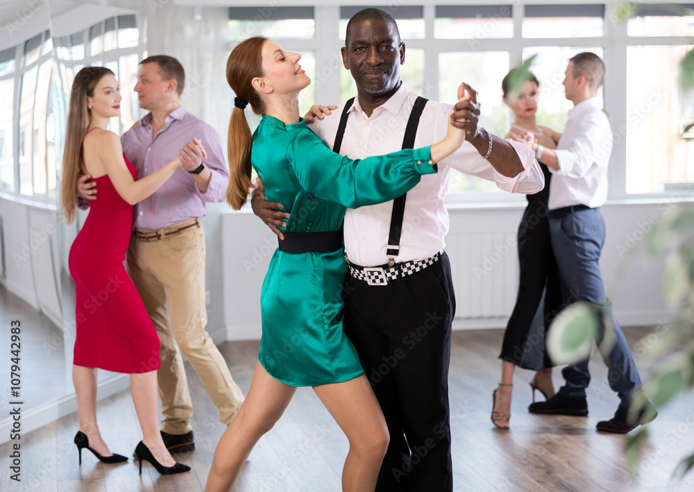 Fototapeta premium During rehearsal of reporting concert, woman with African-American man participants of dance workshop perform figure waltz. Group training and rehearsal, preparation for competitions