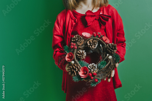 Unrecognizable little girl holding a wreath of pine needles and cones