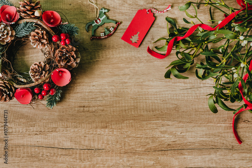 Wreath of pine needles and cones and fresh mistletoe branches with red ribbon bow on wooden background with blank space