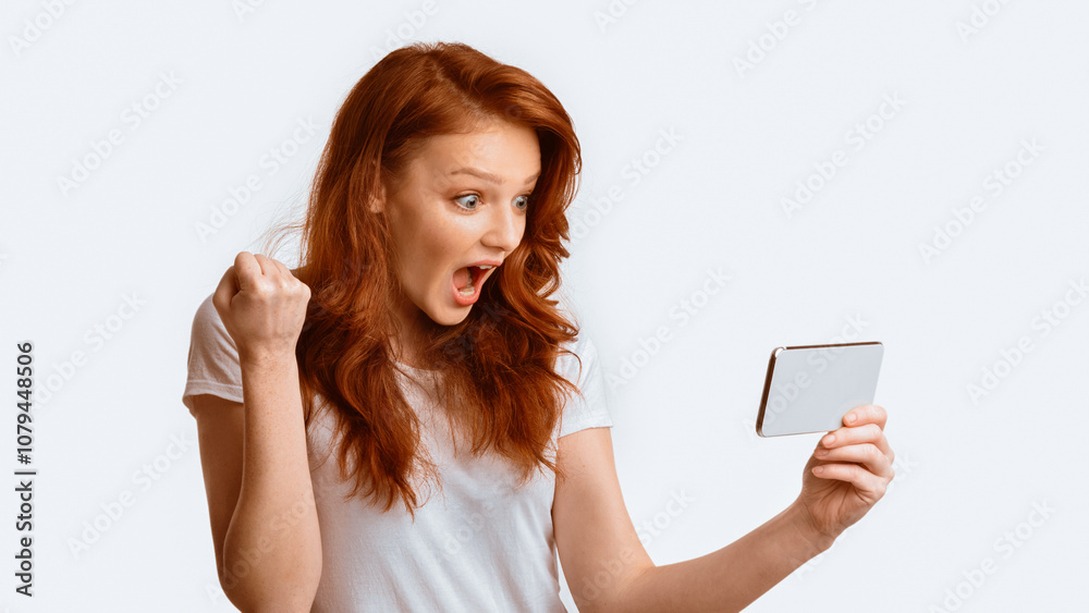Excited Millennial Girl Holding Smartphone Shaking Fists Celebrating Winning Online Game Posing On White Background. Great News. Panorama, Studio Shot Excited Millennial Girl Holding Smartphone Shaking Fists Celebrating Winning Online Game Posing On White Background. Great News. Panorama, Studio Shot